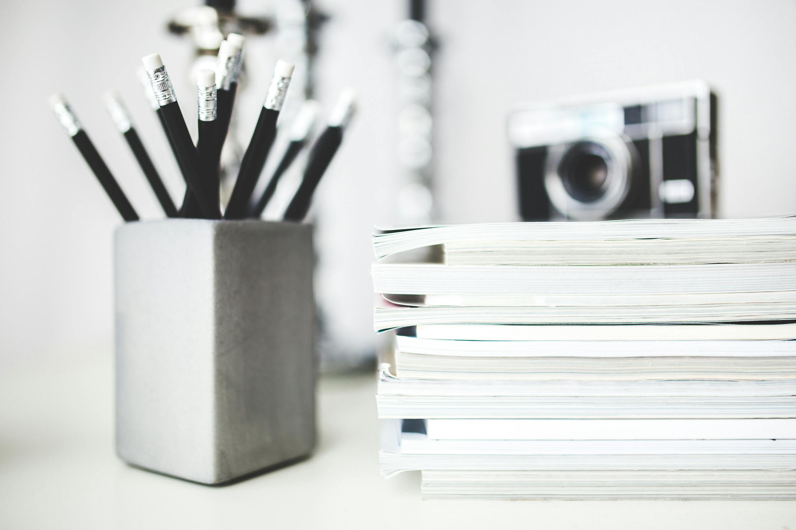 Organized workspace featuring pencils in holder and stacked magazines with a vintage camera in the background.